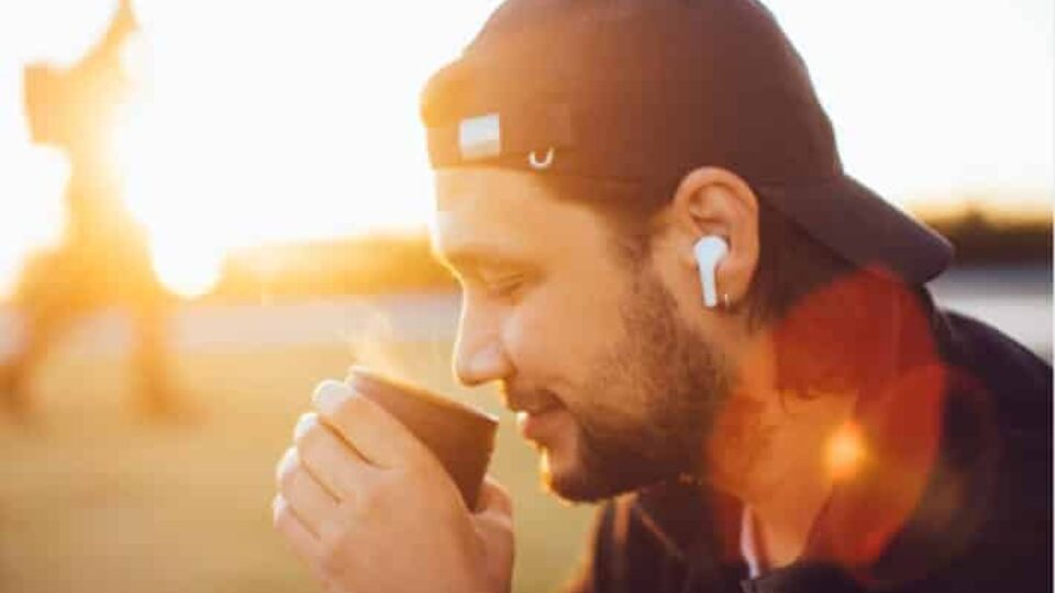 Mann mit Kaffee und EarPods vor der aufgehenden Sonne