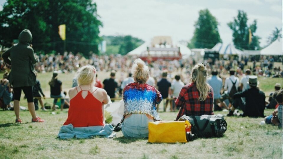 Menschen sitzen auf einem Festival vor der Bühne auf der Wiese.