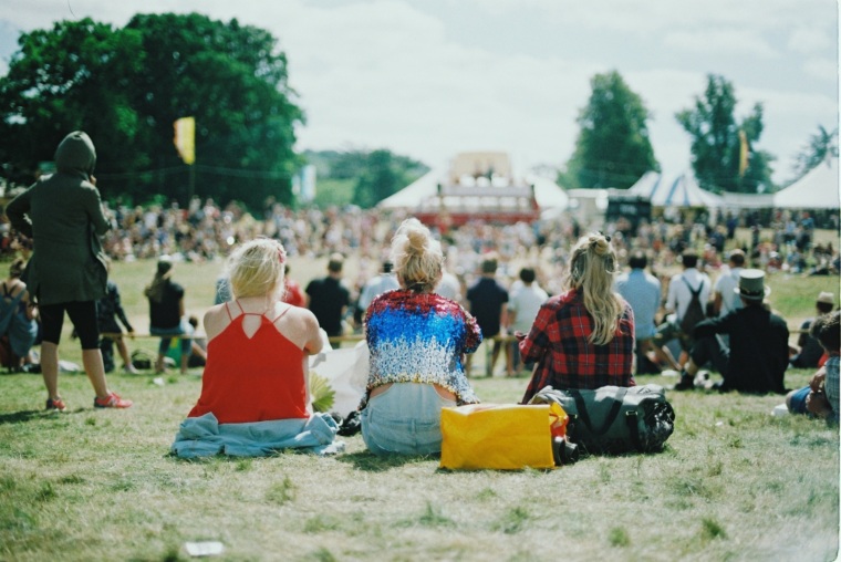 People sitting on the grass in front of the stage at a festival.