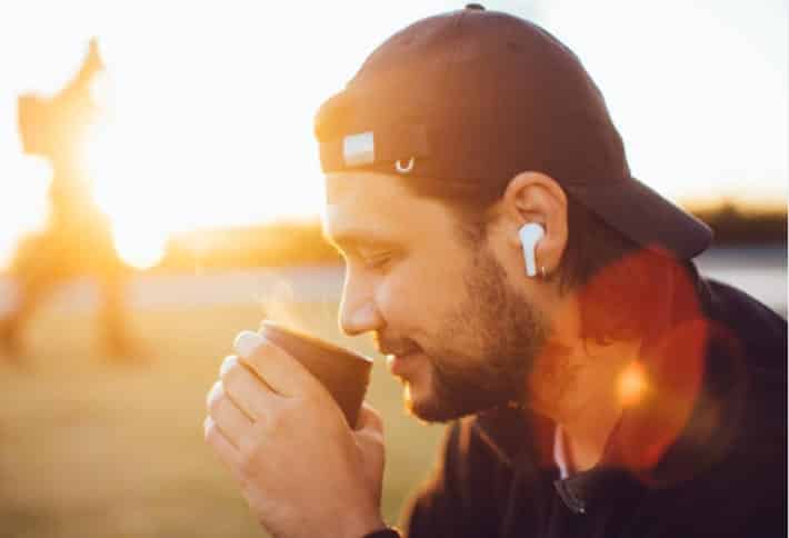 Mann mit Kaffee und EarPods vor der aufgehenden Sonne